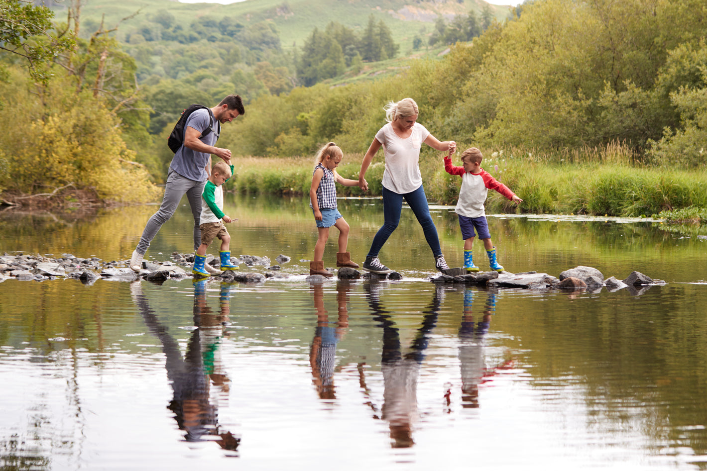 Family crossing river in woods with travel bag.
